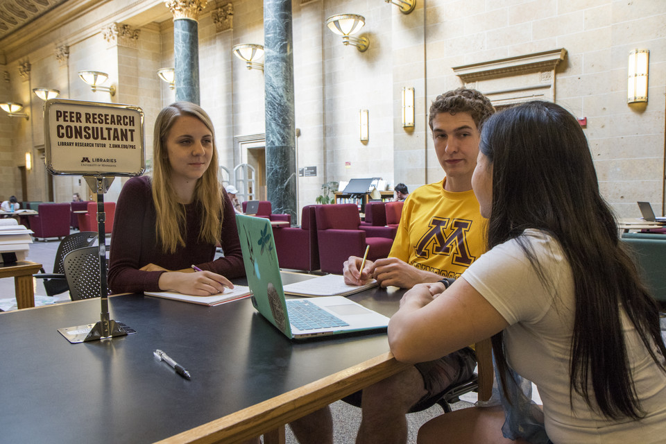 Group of three students in library with sign labeled Peer Research Consultant